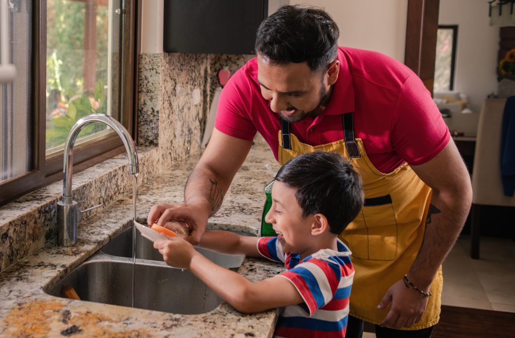 Latino father teaching son how to do dishes